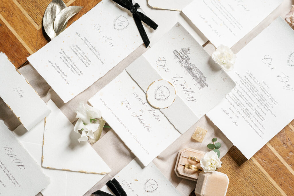 Flatlay von luxuriöser Hochzeitspapeterie mit individuellem Hochzeitslogo auf handgeschöpftem Papier mit Blattgold und handgemalter Illustration