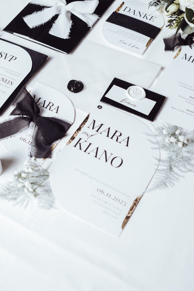 Flatlay einer luxuriösen Hochzeitspapeterie in schwarz Weiss mit hochwertigen Akzenten wie Blattgold, Wachssiegel, Banderole aus Samt & Chiffonband