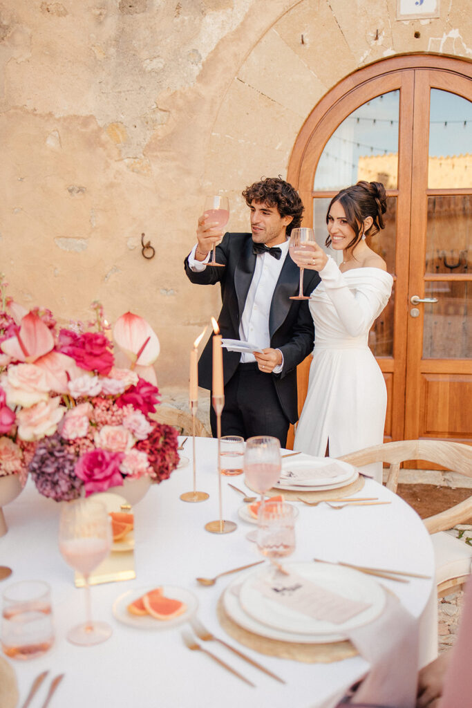 Brautpaar im Innenhof einer Finka auf Mallorca beim Anstossen mit ihren Gästen am Hochzeitstisch