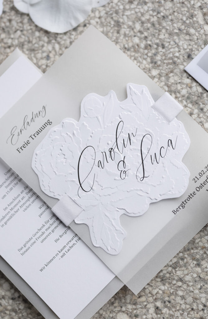Individuelle Hochzeitseinladung mit Blindprägung in Rosenform, passend zur Blumendekoration in elegantem Weiss